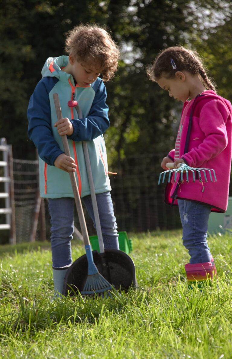 Zwei Kinder helfen mit Rechen und Schaufel auf der Lamaweide.